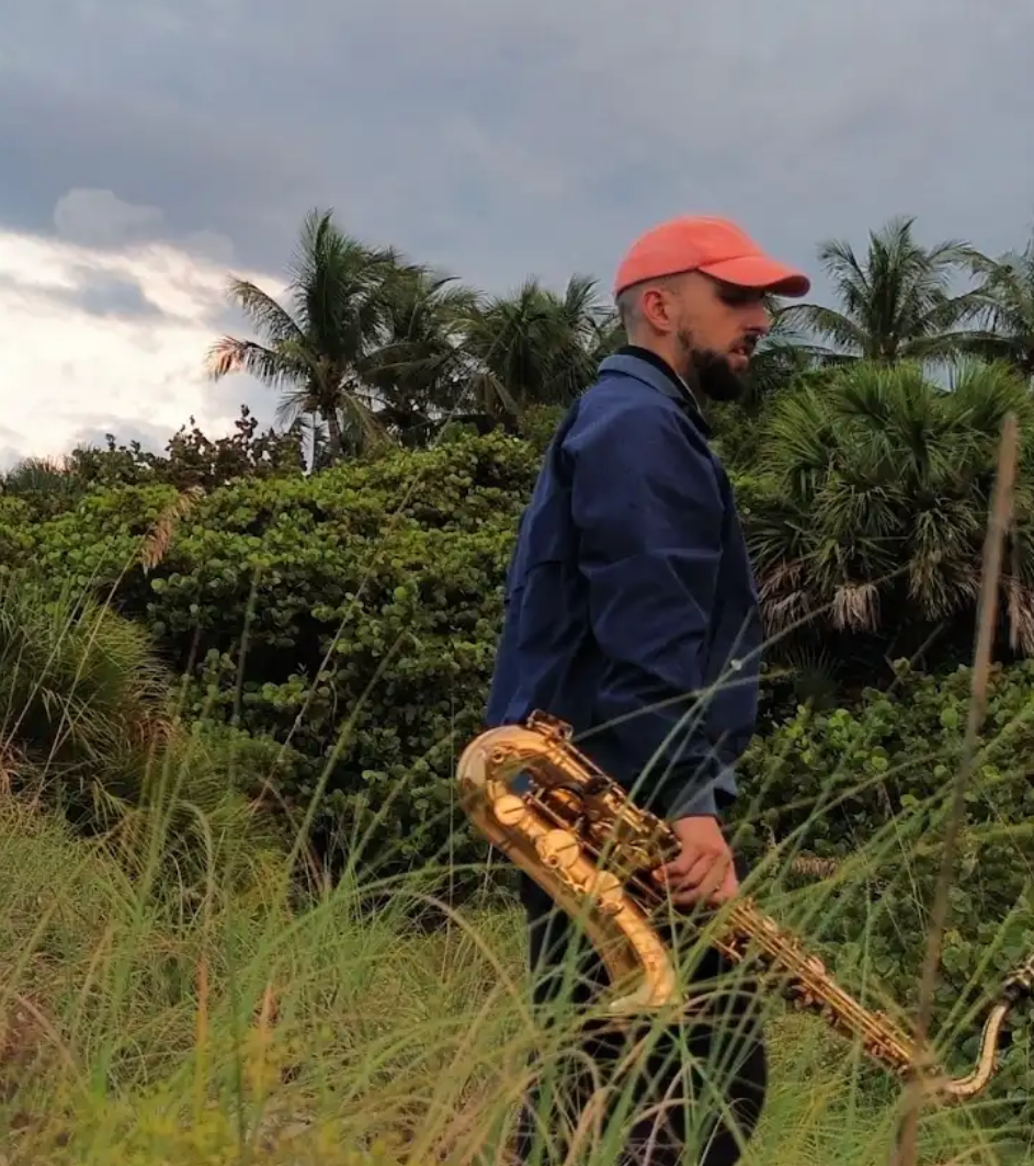 Joel Klein in a grassy field holding a saxaphone