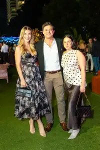 Three attendees posing together on lawn at a lively nighttime event