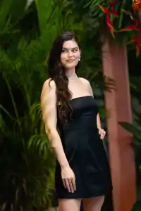 Person in black dress posing among lush green plants at evening event
