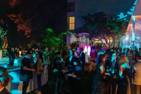 Crowd mingling outdoors with colorful lighting and bar area