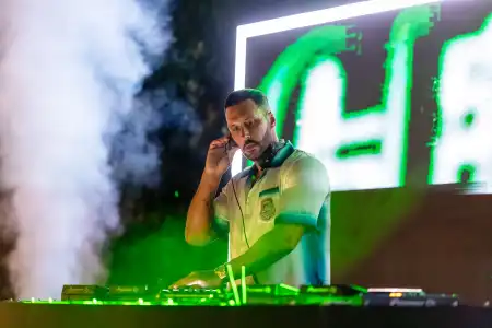 DJ performing with headphones and green lighting, smoke effects behind