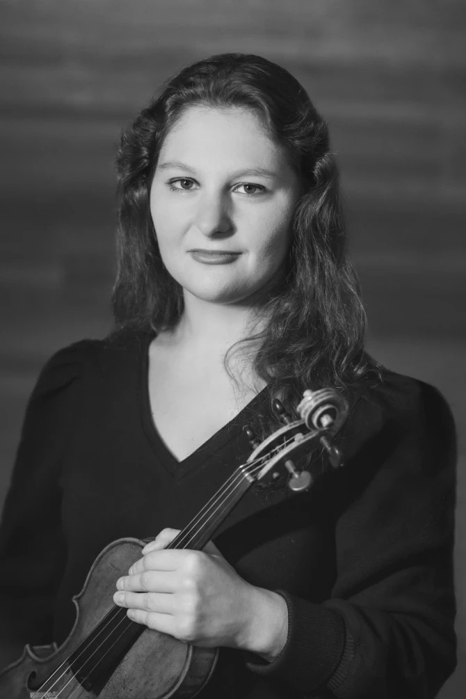 Ilana Zaks Carlin black and white portrait. Holding violin in left hand. wearing a sleeved dark shirt with a "V" cut.
