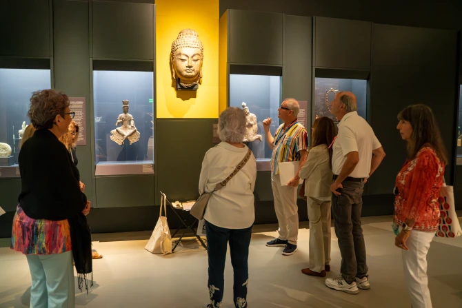 A group of museum visitors gather around a Buddha sculpture as a docent explains it's history and significance
