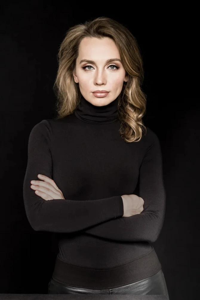Valeria Polunina portrait. arms crossed looking straight into camera. black turtleneck with black pants on a black background.